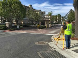 Land surveyor measuring a gated condominium entrance with drive lanes, sidewalks, curbs, and drainage features in Pembroke Pines, Florida.