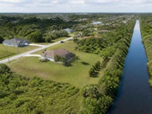 Aerial view of canal side property in Pembroke Pines FL showing residential land, drainage canal, vegetation, and surrounding terrain conditions